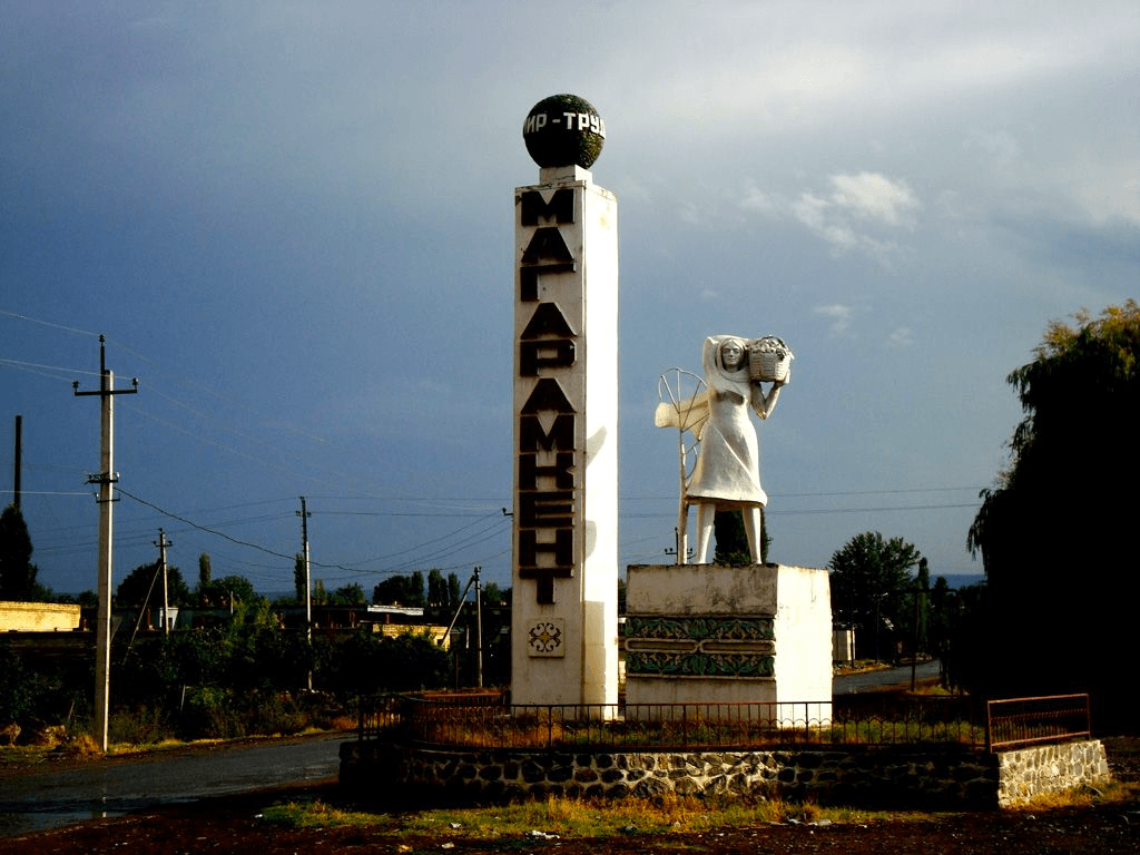 Statue of woman holding a large basket next to tower in city of Margaramkent