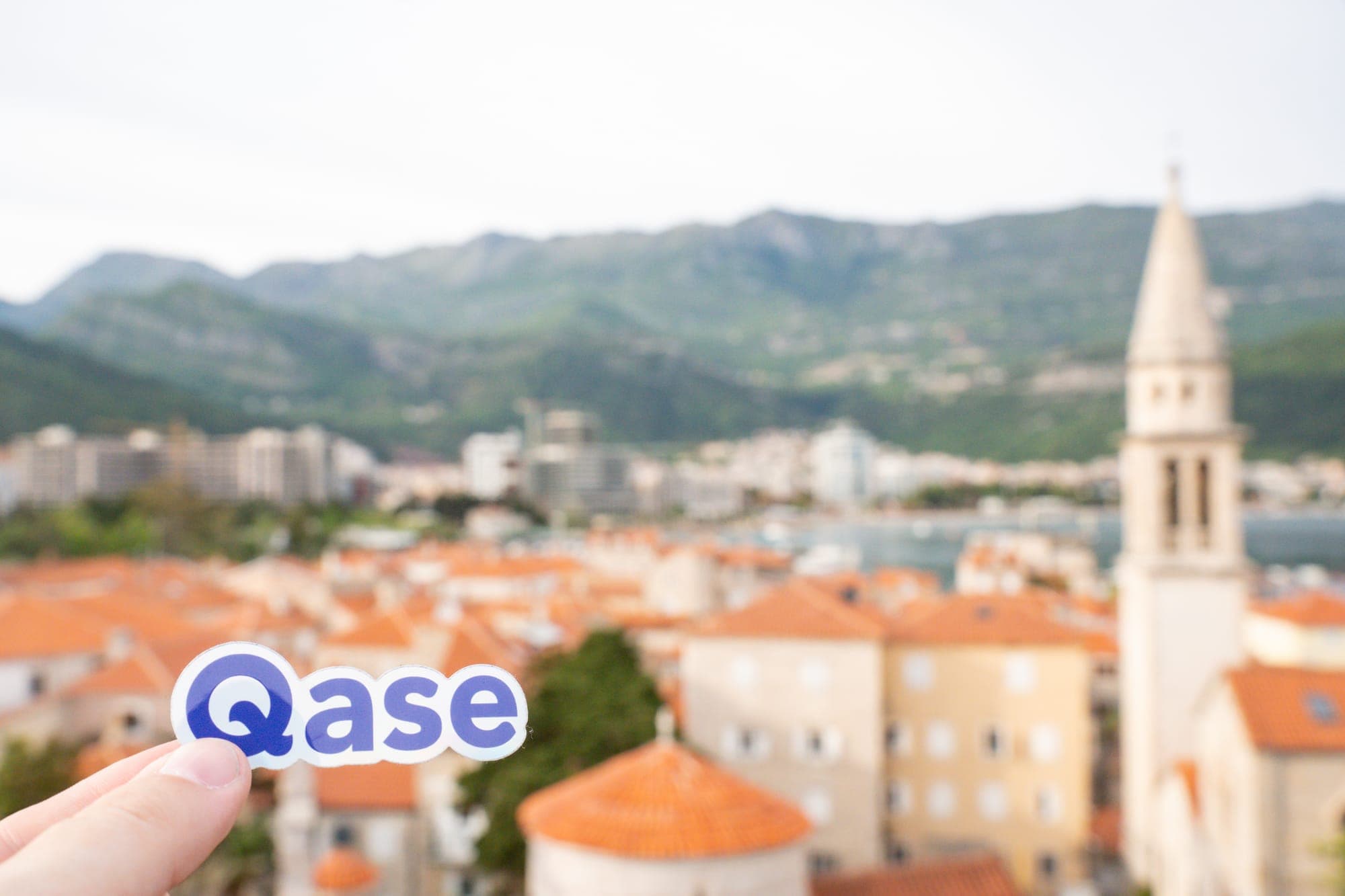 Qase sticker in focus, Budva Montenegro slightly blurred in the background.